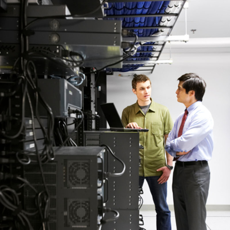 Photo of two men talking and looking at a computer in a data center